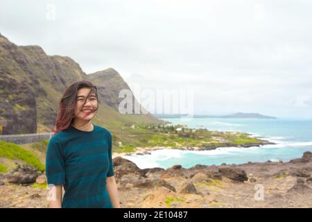 Biracial Asian Caucasian teen girl in piedi alto sopra tropicale hawaiian vista panoramica dell'oceano blu e delle montagne verdi su Oahu, Hawaii con Makapu'u B Foto Stock