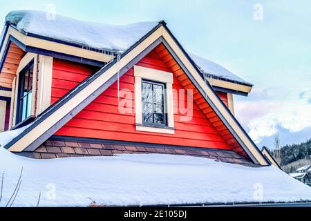 Tetto in tegole innevate su dormitori con finestre e legno rosso muro contro cielo nuvoloso Foto Stock