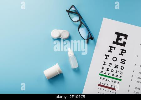 Occhiali con lenti a contatto, gocce e una tabella di prova dell'occhio di Optometrist su uno sfondo blu. La vista dall'alto. Spazio libero Foto Stock