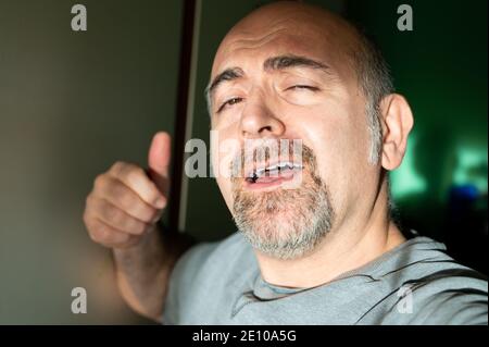 L'uomo caucasico di mezza età prende un autoritratto a casa vicino alla finestra: La luce del tardo pomeriggio illumina il suo volto. Foto Stock