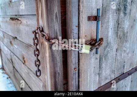 Porta chiusa in legno della stanza da bagno esterna con catena arrugginita e. lucchetto lungo con arco Foto Stock