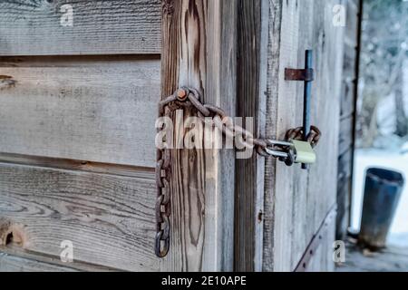 Vecchio bagno esterno in legno fissato con catena arrugginita e lungo lucchetto a grillo Foto Stock