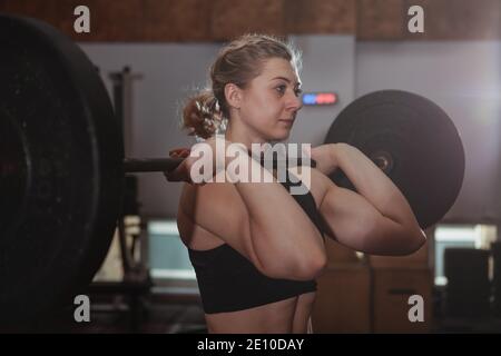 Atleta di crossfit femminile che lavora con il barbell in palestra. Giovane atletica donna che solleva il barbell. Sportiva muscolare con sollevamento di peso allenamento a. Foto Stock