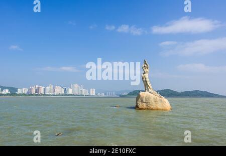 Punto di riferimento della città cinese di Zhuhai. Statua di Fish Woman, fisher ragazza stature con sfondo di mare, isola, e edifici alti Foto Stock