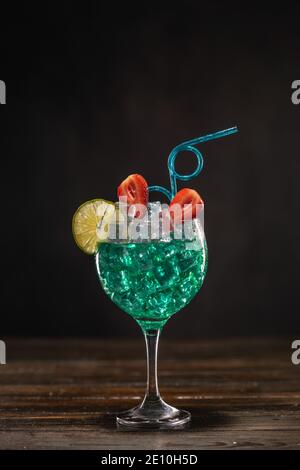 Un cocktail color smeraldo in un vetro di ghiaccio decorato con lime e fragole con una paglia che beve ricci Foto Stock