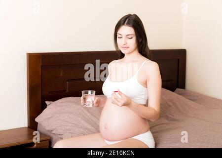 donna che tiene la pillola e un bicchiere di acqua pura fresca. Donne sane millenarie che assumono vitamine antiossidanti della medicina, concetto sanitario. Foto Stock