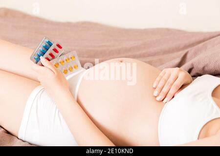 Sezione centrale della donna incinta che prende la pillola di vitamina sul divano a casa. Foto Stock