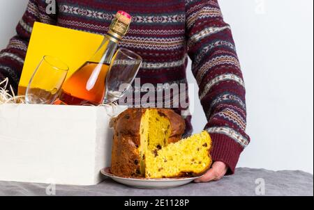 Mano femmina che tiene il panetone pasquale pezzo italiano vicino alla scatola di consegna con bottiglia di champagne. Foto Stock