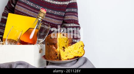 Mano femmina che tiene il panetone pasquale pezzo italiano vicino alla scatola di consegna con bottiglia di champagne. Foto Stock