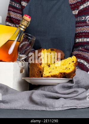 Mano femmina che tiene il panetone pasquale pezzo italiano vicino alla scatola di consegna con bottiglia di champagne. Foto Stock