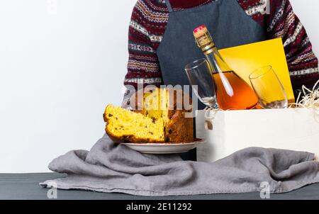 Mano femmina che tiene il panetone pasquale pezzo italiano vicino alla scatola di consegna con bottiglia di champagne. Foto Stock