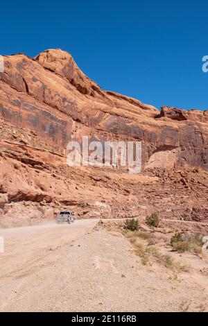 Un camion che guida lungo Kane Creek Road accanto alle torreggianti rocce di arenaria rossa, Moab, Utah, USA Foto Stock