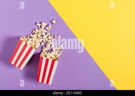 Due secchi di carta a strisce rosse con vista dall'alto del popcorn su sfondo a colori. Alimentazione malsana. Foto Stock