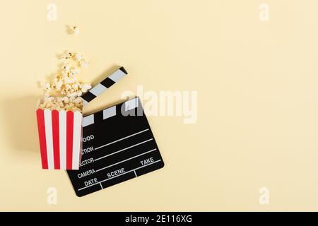 Popcorn in un secchiello a strisce rosse e una vista dall'alto su clapperboard cinematografico su sfondo giallo. Concetto di cinema. Foto Stock