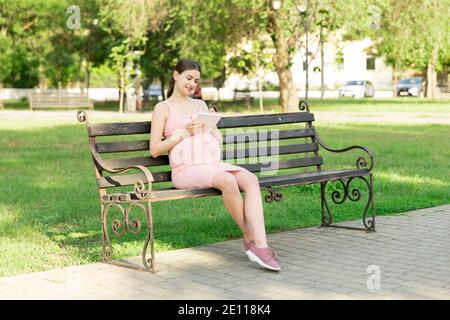 donna incinta si siede su una panchina del parco e scrive una lista da fare all'ospedale. Foto Stock