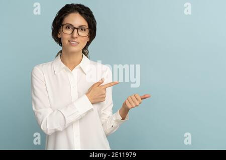 Donna di affari sicura indossa blusa bianca e occhiali che puntano con le dita, mostrando al copy space Foto Stock