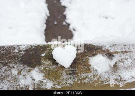Un cuore fatto di neve si trova su una ringhiera in legno, sullo sfondo di un paesaggio invernale con un fiume. Foto di alta qualità Foto Stock