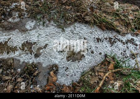 Sfondo invernale astratto, ghiaccio incrinato su puddle ghiacciato. Frammenti di ghiaccio su acqua congelata. Il ghiaccio spezzato pieces.Ice su una pozza d'acqua ghiacciata in inverno Foto Stock