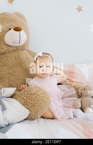 Un bambino carino di un anno si siede circondato da morbido animali giocattoli e tiene la mano sul collo Foto Stock