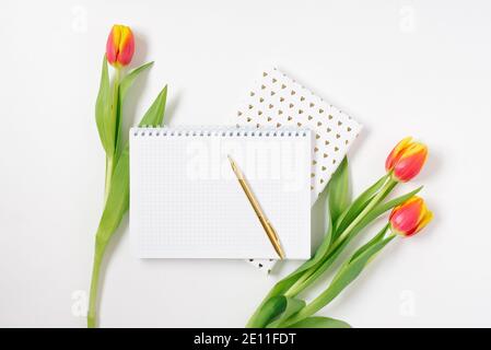 Scrivania da ufficio a piano, stile minimalista su sfondo bianco con spazio vuoto per il testo. Tulipani e taccuini. Blogger's Workplace per San Valentino Foto Stock
