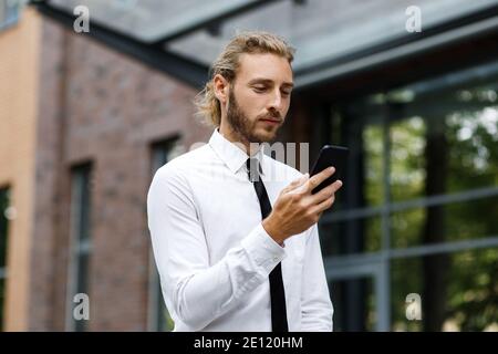 Ritratto di un giovane imprenditore di successo. Un uomo dai capelli ricci in una camicia bianca con un telefono sullo sfondo di un moderno business center Foto Stock