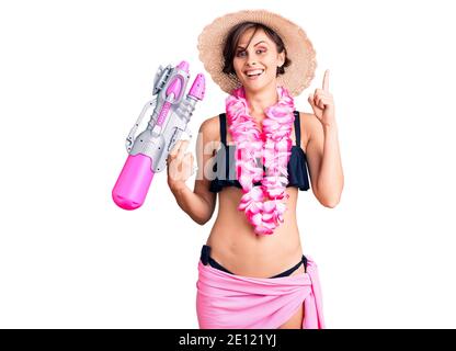 Bella giovane donna con capelli corti indossando bikini e hawaiano lei che tiene la pistola ad acqua sorpreso con un'idea o una domanda puntare il dito con felice Foto Stock