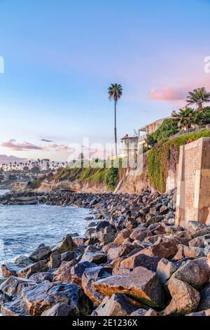 Oceano e costa rocciosa sulla costa con palme contro il cielo blu al tramonto Foto Stock