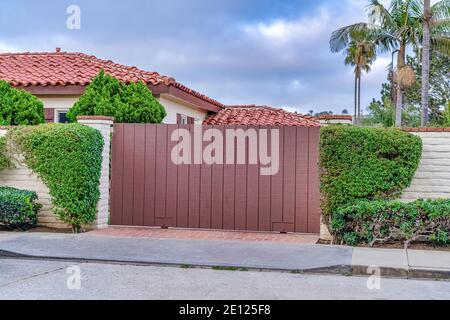 Brown gate and white brick fence against red tile roof of house in San Diego CA Foto Stock