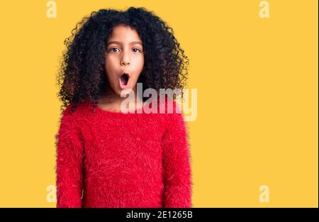 Bambino afroamericano con capelli ricci indossando casual maglione invernale spaventato e stupito con bocca aperta per sorpresa, viso incredulo Foto Stock