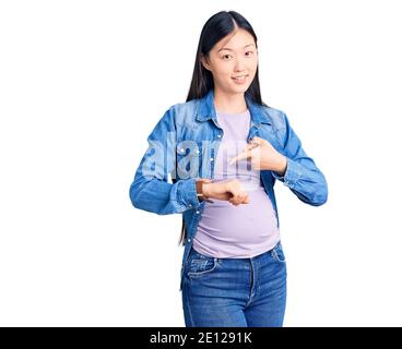 Giovane bella donna cinese incinta in attesa di bambino in fretta indicando il tempo di guardare, impazienza, sconvolto e arrabbiato per il ritardo di scadenza Foto Stock