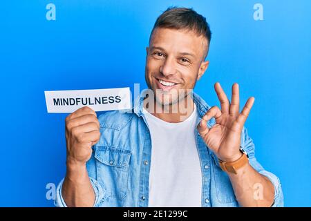 Bell'uomo muscolare tenendo la parola di consapevolezza sulla carta facendo ok segno con le dita, sorridente amichevole gesturing eccellente simbolo Foto Stock