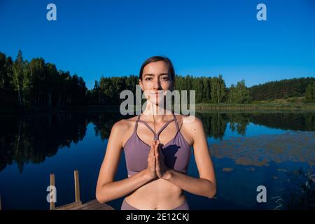 Donna che fa yoga e meditare in un alba all'aperto, tenendo il bastone aroma nelle mani, palme in gesto namaste. Foto Stock