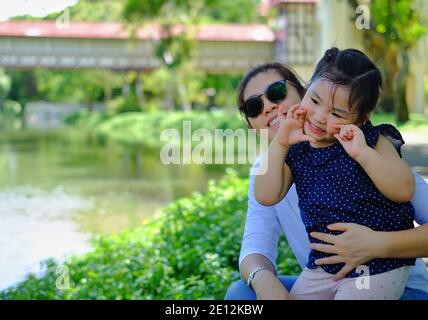 Una madre asiatica e una giovane figlia seduti insieme in un laghetto, guardando i pesci e divertendosi in una giornata di sole. Foto Stock