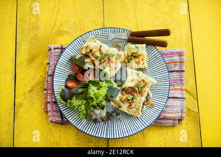 Ravioli svevi con cipolle arrosto e formaggio runny, serviti con insalata su un tavolo di legno giallo Foto Stock