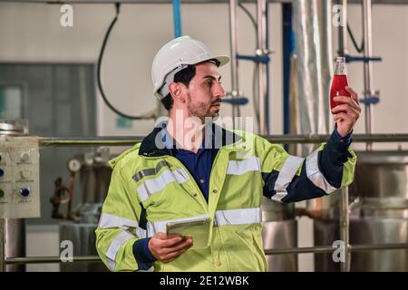 Tecnico addetto che controlla la bevanda nella macchina durante il processo in fabbrica Foto Stock