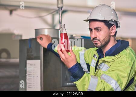 Tecnico addetto che controlla la bevanda nella macchina durante il processo in fabbrica Foto Stock