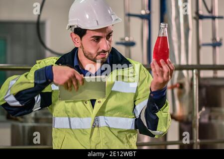 Tecnico addetto che controlla la bevanda nella macchina durante il processo in fabbrica Foto Stock