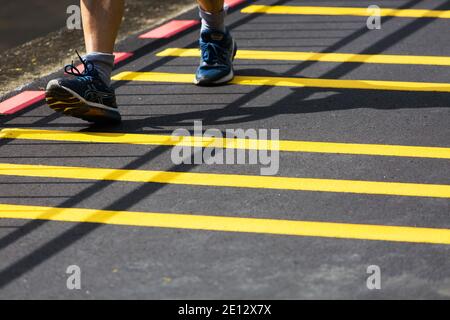 Primo piano di scarpe da running che camminano sul terreno asfaltato con strisce gialle in corrispondenza di un connettore di parcheggio. Singapore Foto Stock