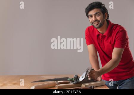 UN GIOVANE FALEGNAME SORRIDENTE ALLA MACCHINA FOTOGRAFICA MENTRE LAVORA Foto Stock