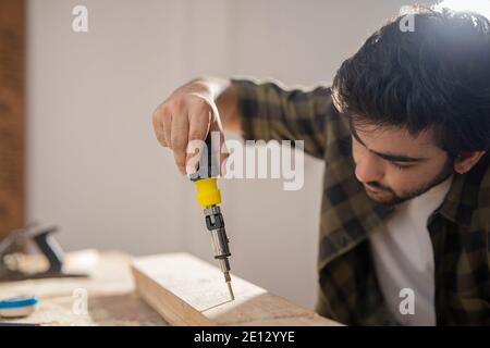 UN CARPENTIERE CHE UTILIZZA UNA MACCHINA PERFORATRICE PER FORARE I BLOCCHI DI LEGNO Foto Stock