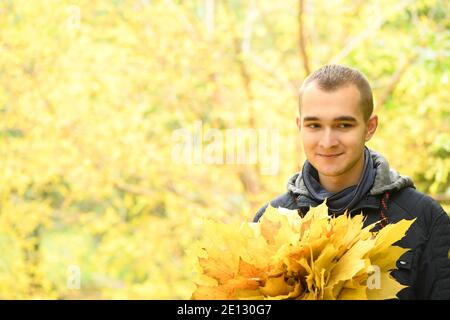 Un uomo tiene in mano un bouquet di foglie d'autunno. Caldo giorno d'autunno, foglie d'autunno gialle. Concetto autunnale. Foto ad alta risoluzione. Foto Stock