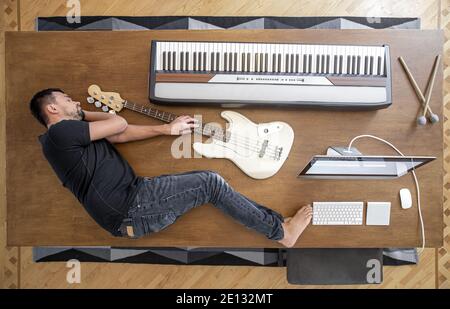 Composizione vista dall'alto con strumenti musicali su un grande tavolo di legno e un uomo. Concetto di creatività musicale. Foto Stock