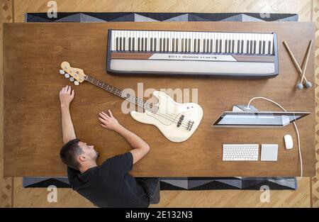 Composizione vista dall'alto con strumenti musicali su un grande tavolo di legno e un uomo. Concetto di creatività musicale. Foto Stock