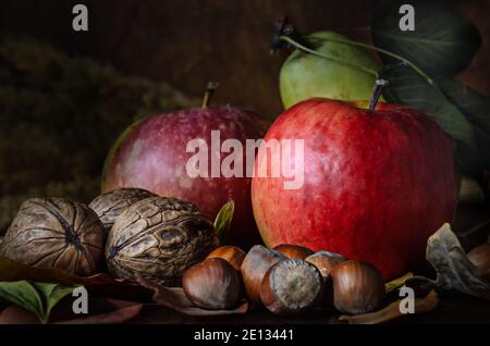 noci e frutta con fogliame in stile rustico al buio sfondo di legno Foto Stock