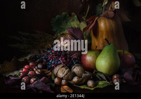 noci e frutta con fogliame in stile rustico al buio sfondo di legno Foto Stock