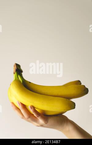 Primo piano a disposizione di una donna caucasica sconosciuta che tiene banane di fronte alla parete bianca - alimenti biologici sani freschi spazio di copia concetto frutta Foto Stock