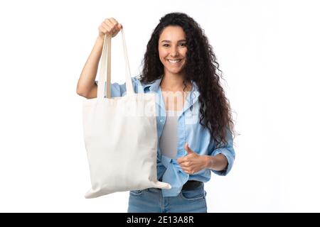 Lady mostrando White Eco Shopper Bag gesturing Thumbs-Up, sfondo bianco Foto Stock