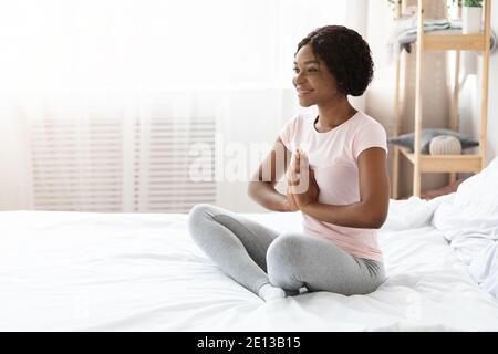 Donna nera sorridente seduta sul letto e meditante Foto Stock