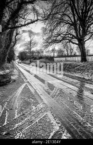 L'uomo e il suo cane camminano lungo una strada di campagna di scongelamento della neve. Foto Stock