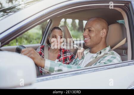 Felice giovane coppia multirazziale guida su strada di campagna, godendo di viaggiare insieme, copia spazio. Bell'uomo africano sorridente, godendo di roadtrip da c Foto Stock